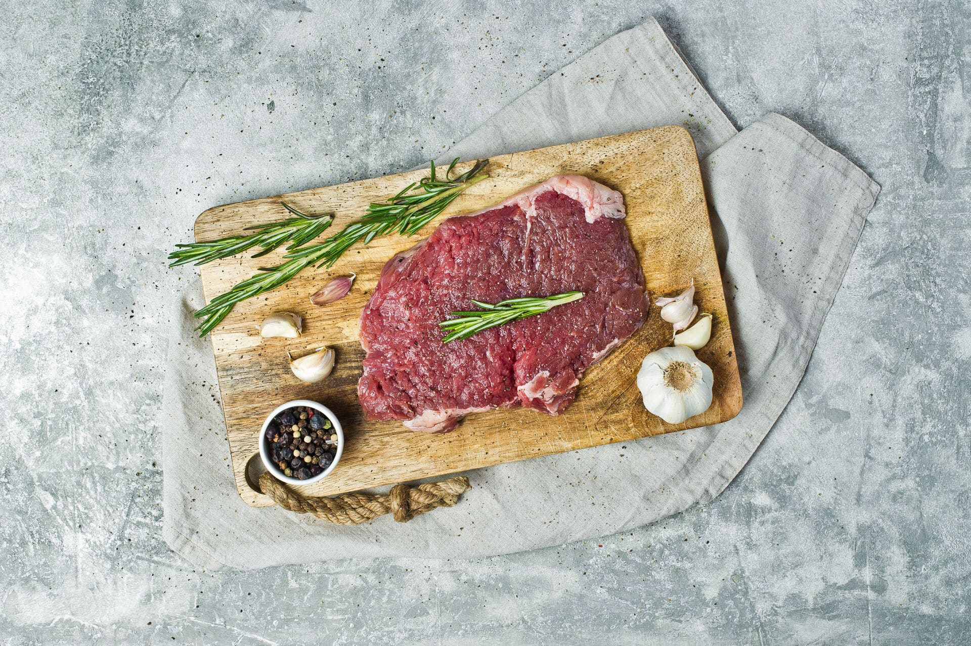 rohes Flank Steak auf einem Steinbrett mit Rosmarin dekoriert